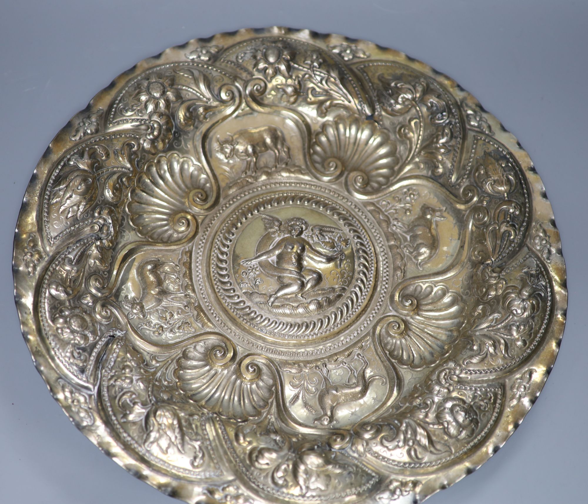A Continental white metal charger, embossed with cherub and animals amid foliage, 44cm, 28oz, (a.f.)